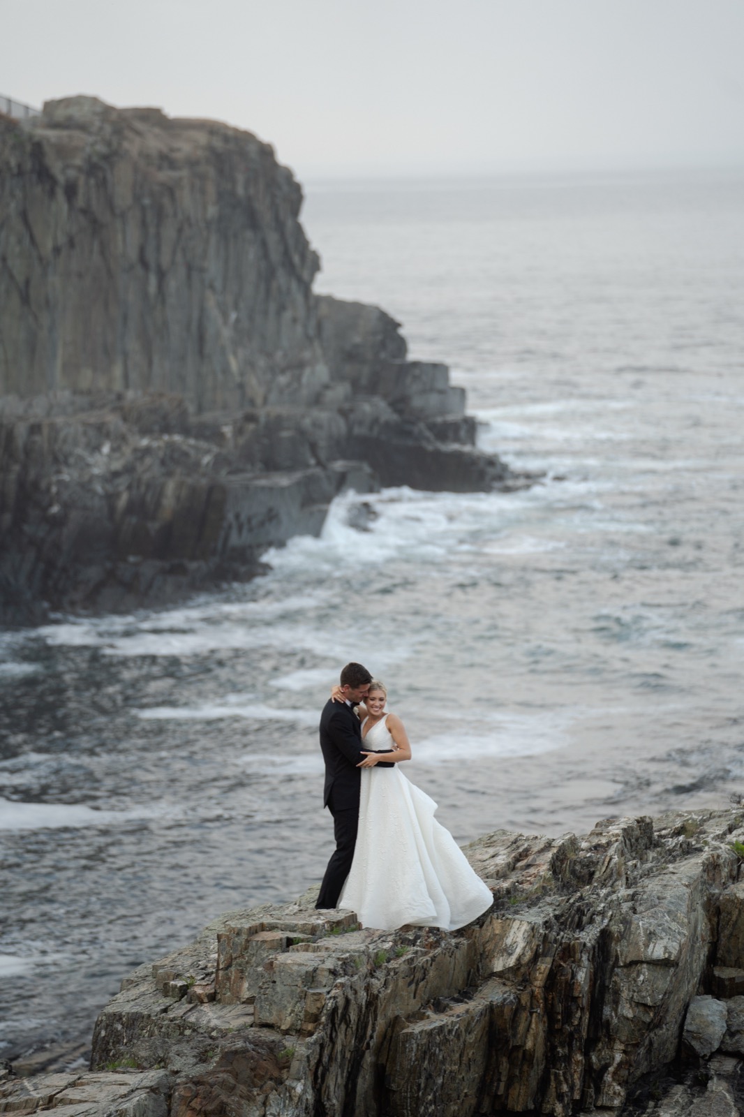 A bride and groom on a rocky sea cliff at dusk